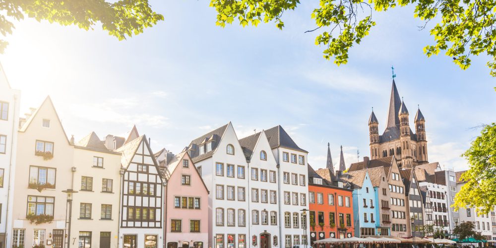 Houses and park in Cologne, Germany Houses and park in Cologne, Germany. Many of them are colourful, they are facing a public park with green grass and some trees. There is a bell tower on background. Travel and architecture concepts.